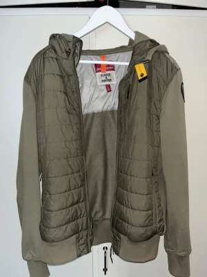 PARAJUMPER CARDIGAN - Snygg olivgrön pufferjacka från Parajumpers med quiltade partier och huva. Jackan har dragkedja framtill, ribbade muddar och en patch på ärmen. Nypris ca 4000kr. Strl L passar M.