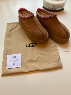 Bruna UGG tofflor i mocka - Ett par Ugg Tasman tofflor i en brun färg. Skorna kommer med en tillhörande dustbag i storlek 39. Säljer dom för 900kr   Skickar paketet samma dag eller dagen efter.