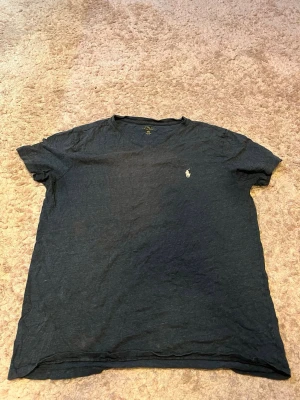 Mörkgrå t-shirt från Polo Ralph Lauren - Klassisk mörkgrå t-shirt från Polo Ralph Lauren med den ikoniska loggan broderad på bröstet. T-shirten har korta ärmar och rund halsringning. Tillverkad i mjuk bomull som känns skön mot huden. Perfekt basplagg till garderoben.