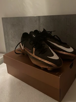 Nike Phantom GT fotbollsskor svart/koppar - Nike Phantom GT worldcup 2022 special edition fotbollsskor i svart med vita och kopparfärgade detaljer. Skorna har snörning och en låg profil med platt sula och greppvänliga dobbar. Perfekta för dig som vill ha kontroll och stil på planen. Pris kan diskuteras och de rengörs vid köp! 
