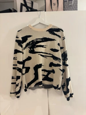 Beige tröja med svart abstrakt mönster - Trendig beige tröja med svart mönster från Pieces i storlek S. Tröjan har rund halsringning med ljus ribbad kant och långa ärmar. 