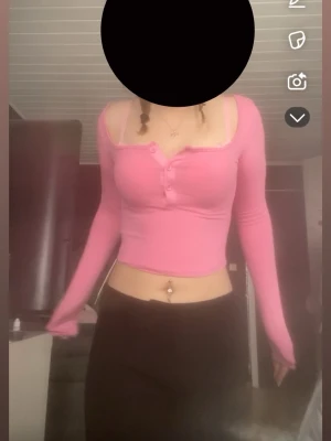 Rosa croppad ribbad topp - Trendig rosa croppad topp med lång ärm och ribbad struktur. Toppen har knappar framtill och en djup v-ringning som ger en snygg och ungdomlig look. Perfekt för dig som vill ha en färgglad och bekväm topp till din outfit.