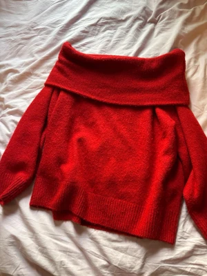 Röd offshoulder stickad tröja - Säljer en röd stickad tröja med bred offshoulder-krage. Tröjan har långa ärmar och ribbade muddar vid ärmslut och nederkant. Perfekt för dig som vill ha en mysig och trendig look i höst och vinter.