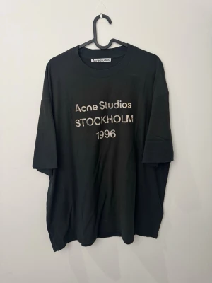 Svart Acne Studios t-shirt - Cool svart t-shirt från Acne Studios med trycket 'Acne Studios STOCKHOLM 1996' på bröstet. Oversized passform och klassisk rund halsringning. Perfekt för en avslappnad streetwear-look.