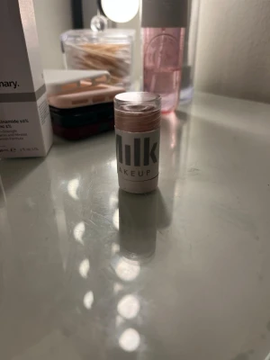 Milk Makeup highlighter stick - Highlighter stick från Milk Makeup i en krämig formula. Kommer i en kompakt, rund förpackning med transparent lock och vit etikett. Färgen är en skimrande champagne/ljusrosa ton som ger glow till huden.