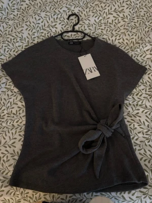 Zara topp med knut, S - Säljer en mjuk topp med knut från Zara. Den är oanvänd med prislapp kvar. Den gråa färgen är slutsåld på hemsidan.