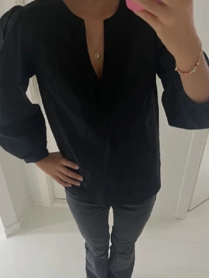 Svart blus med v-ringning - Stilren svart blus med v-ringning och puffiga långärmar. Blusen har en avslappnad passform och fina detaljer vid axlar och ärmar. Perfekt till utgång, fin middagar, eller vardags💓🩷