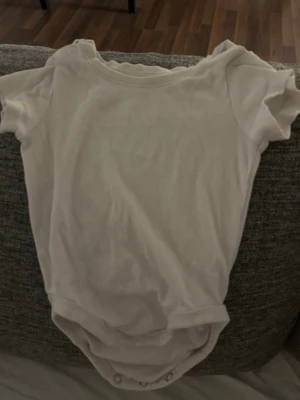 Bebis kläder Vit kortärmad body från H&M - En basic vit kortärmad body från H&M i mjuk ekologisk bomull. Modellen har tryckknappar i grenen och vid axeln för enkel påklädning. Perfekt till vardags och enkel att matcha med andra plagg.
