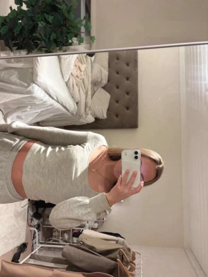 Grått loungewear-set med långärmad topp - Mysigt loungewear-set i ljusgrått med långärmad, croppad topp och matchande byxor. Setet har en enkel och stilren design, perfekt för avslappnade dagar hemma. Materialet ser mjukt och stretchigt ut för maximal komfort.