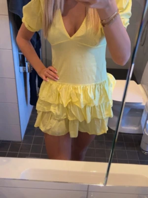 Gul volangklänning från Meet Me There - Säljer en söt gul kortklänning från Meet Me There i storlek S/M. Klänningen har puffärmar, djup v-ringning och flera lager volanger i kjolen. 