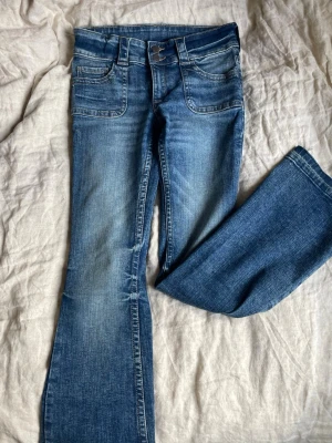 Blå bootcut jeans från H&M - Snygga blå bootcut jeans från H&M med låg midja och justerbar midja. Jeansen har klassiska fem fickor och slitningar framtill för en cool look. Materialet är bomull med lite stretch för extra komfort. Skriv om ni har andra frågor!🥰