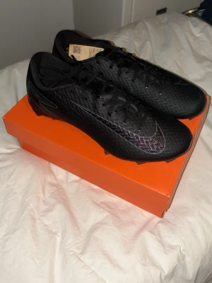 Nike Mercurial fotbollsskor - Säljer ett par svarta Nike Mercurial fotbollsskor med stilren design och diskret Nike-logga på sidan. Skorna har snörning och är tillverkade i ett lätt syntetmaterial som ger bra bollkontroll och grepp på planen. Helt oanvända med lappen kvar. Skorna säljes pga för små. 