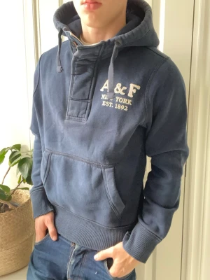 Abercrombie and fitch hoodie med knappar - Abercrombie and fitch hoodie med knappar med en sorts design som ska vara vintage typ. Där dom flesta av kanterna på plagget är slitna. Inga defekter! Modellen i bilderna är 180 cm 75 kg och bär Storlek L stor på modellen, Kom med frågor! 🌟 (Kan gå ned i pris vid köp av paket 😉) 