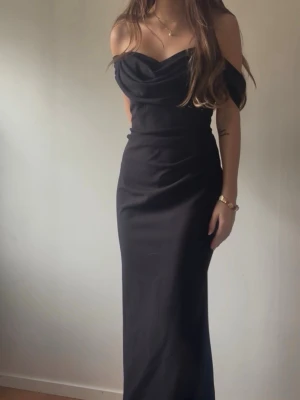 Svart offshoulder långklänning - Svart långklänning med offshoulder-design och draperad urringning från Bubbleroom. Oanvänd och köpt för 880kr. Aldrig använd då jag valde en annan balklänning. Jag är 165 cm lång och den är perfekt i längden, speciellt med klack. Klänningen har en figurnära passform och är tillverkad i ett mjukt, följsamt material och en inbyggd gömd ”korsett” liknande del på magen. Skriv för fler bilder 🩷Pris går att diskutera vid snabb affär 