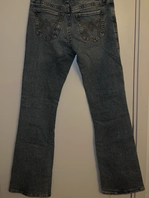 Lågmidjade Bootcut jeans med broderade bakfickor - Ett par ljusblå bootcut jeans med snygga broderade detaljer på bakfickorna. Jeansen har klassisk femficksdesign, låg midja och är tillverkade i denim. Perfekta för dig som gillar en avslappnad men trendig look. Endast använda 1-2 gånger.