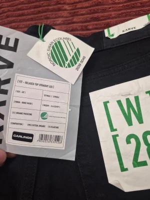 Svarta raka jeans från Karve relaxed top straight leg W28 - Snygga svarta jeans från Karve med relaxed top och raka ben. Jeansen har ekologisk bomull, lite stretch och klassisk femficksmodell. Märkta med Nordic Swan Ecolabel och har en clean rinse wash finish. Perfekta för dig som gillar enkel och stilren look.