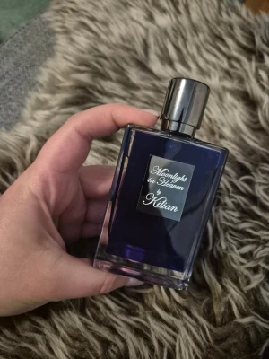 Moonlight in Heaven parfym från Kilian - Moonlight in Heaven från Kilian är en lyxig parfym i en mörkblå, rektangulär glasflaska med silverfärgat lock och metallisk etikett framtill. Flaskan har en elegant och modern design som känns exklusiv och stilren.