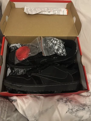 Air Jordan 1 OG TS Travis scott Black Phantom sneakers  - Travis scott sneakers i svart med vita kontrastsömmar och bandanamönster. Skorna kommer med extra skosnören i rött och svartvitt mönster. Perfekt för dig som gillar streetwear och unika detaljer. Skorna är i storlek 42,5 men är små i storleken så jag skulle säga att de är i typ storlek 41,5/42. Skorna är varken creasade eller slitna 