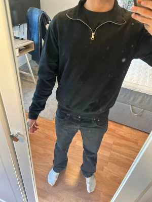 Svart half-zip hoodie - Säljer en svart hoodie med half-zip dragkedja och hög krage. Hoodien har en clean look utan tryck, ribbade muddar vid ärmslut och nederkant samt är tillverkad i mjukt sweatshirtmaterial. Perfekt för en avslappnad och stilren outfit.