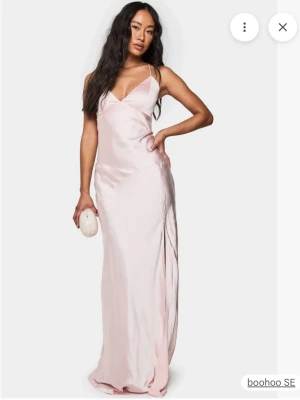 Ny med prislapp! Ljusrosa långklänning - Aldrig använd! Säljer en elegant ljusrosa långklänning  i glansigt satinliknande material. Klänningen har smala axelband, djup v-ringning och öppen rygg med snygg snörning. Perfekt för dig som vill ha en stilren och trendig look.