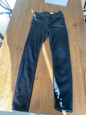 Svarta skinny jeans från Tiger of sweden - Säljer ett par svarta skinny jeans från Tiger of Sweden med klassisk femficksdesign och hög midja. Jeansen har smal passform och är tillverkade i stretchigt denimtyg för extra komfort. Perfekta för en clean och stilren look.