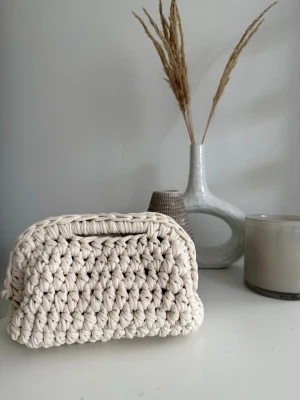 Beige virkad liten necessär - Superfin egengjord virkad clutch väska. Färgen är mer åt det benvita hållet. Bygeln är 18 cm och trots att väskan är liten så rymmer det dagliga behov. Den har handtag för att lättare kunna bära väskan. Om det finns lite små synliga detaljer som kan se ”fel” ut beror det på att väskan är ett hantverk, alla väskor blir inte identiska.  Priset är satt efter tidsåtgång och materialets kostnad🥰 Kan acceptera bud vid snabb affär!  Hör gärna av er om ni har frågor
