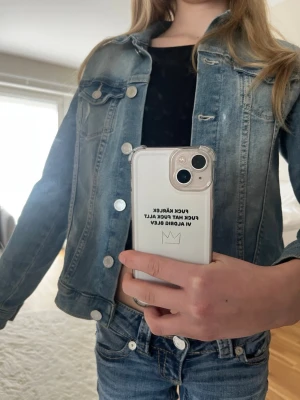 Blå klassisk jeansjacka - Snygg blå jeansjacka med slitna detaljer och silverfärgade knappar. Jackan har två bröstfickor med lock och knapp samt raka ärmar. Perfekt att slänga över en t-shirt för en avslappnad look.