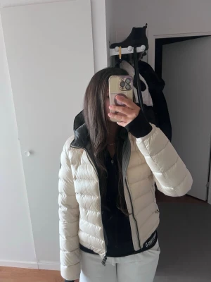  Colmar jacka - Säljer en snygg vit pufferjacka från Moncler med svart innerfoder och huva. Jackan har en klassisk quiltad design, dragkedja framtill och Moncler-logga på ärmen. Perfekt för kalla vinterdagar och riktigt trendig look.