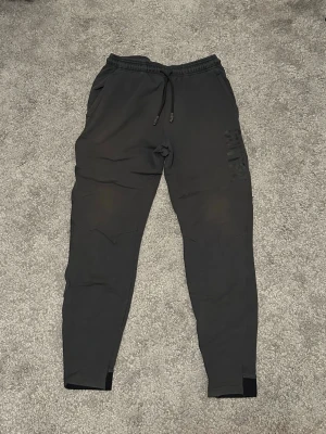 Svarta mjukisbyxor från Contra - Säljer ett par svarta mjukisbyxor från Contra med trycket 'CONTRA SPORT TOGETHER AGAINST TIME' på benet. Byxorna har dragsko i midjan, muddar vid bensluten och sidofickor. Perfekta för chill eller träning.