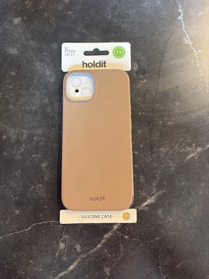 Beige silikonskal Holdit iPhone 14/13 - Snyggt och stilrent beige silikonskal från Holdit som passar iPhone 14 och 13. Skalet är tillverkat i mjukt silikon som ger ett bra grepp och skyddar mobilen mot stötar. Slimmad design och stöd för trådlös laddning. 