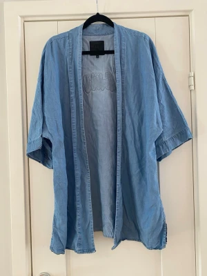 Ljusblå denim kimono  - Ljusblå kimono med broderad text "Glamour" på ryggen. Kimonon har vida ärmar och sprund i sidorna.  Använd men i fint begagnat skick   Mått Över bröstet: ca 62 cm Längd från axeln och ner: ca 80 cm  100% lyocell   Kommer från ett djur och rökfritt hem