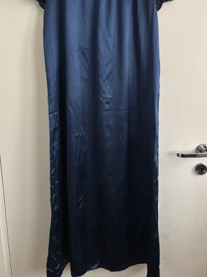 Mörkblått långt nattlinne i satin - Snyggt och elegant nattlinne i mörkblå satin med lång, rak passform. Materialet är glansigt och mjukt, vilket ger en lyxig känsla. Perfekt för dig som vill ha något bekvämt och stilrent att sova i.