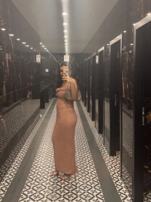 Glittrig champagnefärgad långklänning - Säljer en glittrig långklänning i champagnefärg med figurnära passform. Klänningen är axelbandslös och har en snygg drapering över bysten. Perfekt för dig som vill sticka ut på festen!