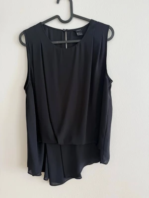 Svart Elegant Blus - Stilren och snygg svart blus från Lindex med fint fall och lager-på-lager känsla framtill. Perfekt både till vardag och fest!  ✨ Märke: Lindex ✨ Storlek: 40 ✨ Material: 100% polyester ✨ Skick: Väldigt fint skick  En klassisk och tidlös topp som passar till allt – jeans, kostymbyxor eller kjol!