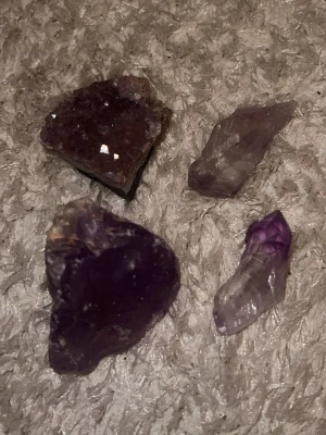 Fyra ametistkristaller och mineraler - Säljer fyra olika ametistkristaller och mineralbitar i olika former och storlekar. Färgerna varierar från djup lila till ljusare violett och en av bitarna har en glittrande yta. Perfekt för dig som gillar kristaller eller vill dekorera ditt rum.