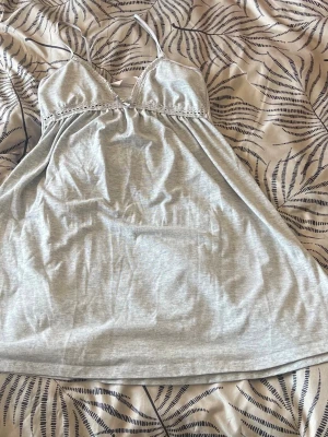 Ljusgrått nattlinne med spetsdetalj - Sött ljusgrått nattlinne med tunna axelband och spetskant vid bysten. Mjuk och skön trikå som faller fint och ger en avslappnad känsla. Perfekt för mysiga kvällar hemma. Ingen synlig logga eller märke.