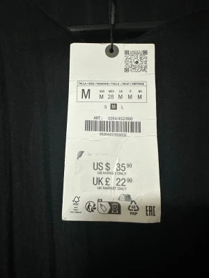 Svart plisserad blus från Zara - Trendig svart blus från Zara med plisserad struktur och rund halsringning. Blusen har korta ärmar och en avslappnad passform som ger en cool och modern look. Perfekt att styla med både jeans och kjol för en snygg outfit.