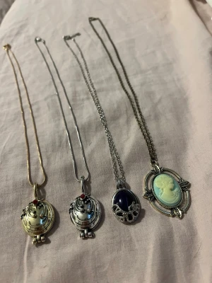 Elena Gilbert and Katherine pierce halsband - Säljer fyra halsband med unika hängen: två silver- och guldfärgade medaljonger med röda stenar, ett silverfärgat halsband med mörklila sten och dekorativa detaljer samt ett antikguldigt halsband med en klassisk cameo i ljusgrönt och vitt. Perfekta för dig som gillar retrostil.