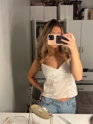 Vit sidenlinnetopp med spetsdetaljer - Säljer en vit linnetopp i siden med tunna axelband och fina spetsdetaljer vid urringningen. Den är jätte fin till lång kjol eller jeans. Säljer pga att jag har flera sånna liknande. Den är använd 3 gånger max. 