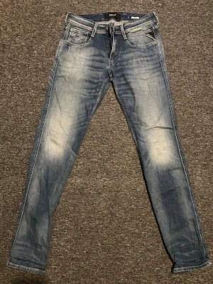Replay anbass jeans - Säljer ett par blå jeans från replat Jeans med snyggt slitna detaljer och klassisk femficksmodell. Jeansen har ljusare partier framtill och bakficka med dekorativ söm samt små röda detaljer. Tillverkade i bomull med en rak passform.