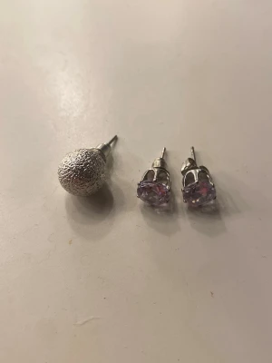 Örhängen i silver - Säljer ett set med tre örhängen i silverfärg. Ett är en rund, glittrig kula och de andra två är klassiska stift med ljuslila stenar i fattning. Perfekt för dig som gillar att mixa olika stilar och former. Materialet ser ut att vara metall och glas. 10kr/st, 1 par för 15, alla 3 örhängen 20kr💕