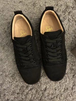 Svarta sneakers från Christian Louboutin - Stilrena svarta sneakers från Christian Louboutin med klassisk låg profil. Skorna har ovandel i mocka och släta svarta skosnören. Insidan är beige och märket syns tydligt på innersulan. Perfekta för dig som gillar exklusiva och tidlösa sneakers. Med kommer skolåda, skopåse. Använda endast 2 gånger!! Priset är diskuterbart😄