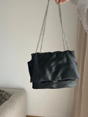 Svart axelväska - Stilren svart axelväska i mjukt material med dubbla silverfärgade kedjeremmar i fint skick!💕