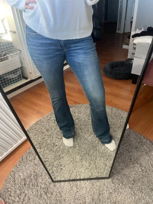 Blå bootcut jeans i klassisk denim - Säljer ett par blå bootcut jeans i klassisk denim med lätt slitning på låren. Jeansen har normal midja och är i ett mjukt, stretchigt material som sitter snyggt över höfterna och låren. Perfekta för dig som gillar en tidlös och avslappnad stil. Uppsprättade längst ner. OBS finns ett hål på sidan av midjan, skriv så skickar jag bild!