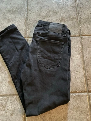 Svarta slim fit jeans Jack & Jones - Svarta slim fit jeans från Jack & Jones med klassisk femficksdesign och normal midja. Jeansen har en stilren look och är tillverkade i stretchigt material för extra komfort. Perfekta för en trendig och avslappnad stil.