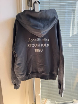 Svart hoodie från Acne Studios - Snygg svart hoodie från Acne Studios med tryck på ryggen där det står 'Acne Studios STOCKHOLM 1996'. Klassisk modell med huva och ribbade muddar. Perfekt för en avslappnad och trendig stil.