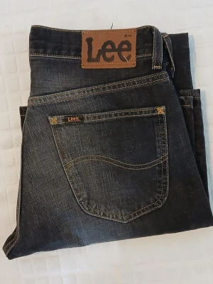 Blå bootcut jeans från Lee - Säljer ett par klassiska blå bootcut jeans från Lee med fem fickor och knappgylf. Jeansen har en snygg tvätt med ljusa slitningar och breda ben. Perfekta för dig som gillar en retrostil och vill ha ett par jeans med skön passform.
