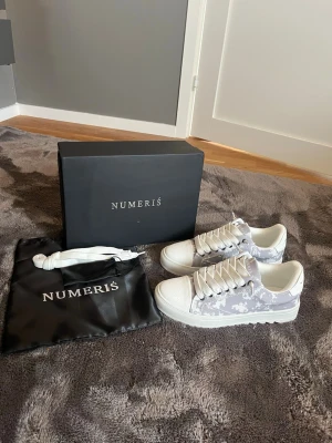 Numeris skor  - Snygga sneakers från Numeris i vitt och ljusgrått camomönster. Skorna har tjock vit sula, breda vita skosnören och detaljer i textil och syntet. Perfekta för dig som vill sticka ut med en modern och trendig look. Skriv gärna vid frågor :)
