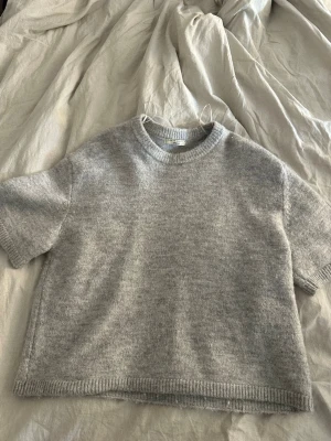 Kortärmad stickad  - Mysig grå stickad t-shirt med korta ärmar och rund halsringning. Tröjan har en avslappnad passform och ribbstickade kanter vid ärmslut och nederkant. Perfekt för lager-på-lager och chill stil.