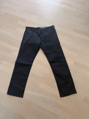 Svarta raka matinique jeans - Martinique svarta jeans/chinos i stilren och modern design. Modell “Slim Fit / Narrow Leg” med smal passform och raka, rena linjer som passar både till vardag och mer uppklädda outfits. Tillverkade i mjukt stretchmaterial för hög komfort och bra rörelsefrihet. Diskreta detaljer med ton-i-ton sömmar och svart logopatch baktill ger ett exklusivt uttryck.  Helt nya  * Märke: Martinique * Modell: Slim Fit / Narrow Leg * Färg: Svart * Storlek: W35 / L36 * Material: 46% bomull, 38% elastomultiester, 